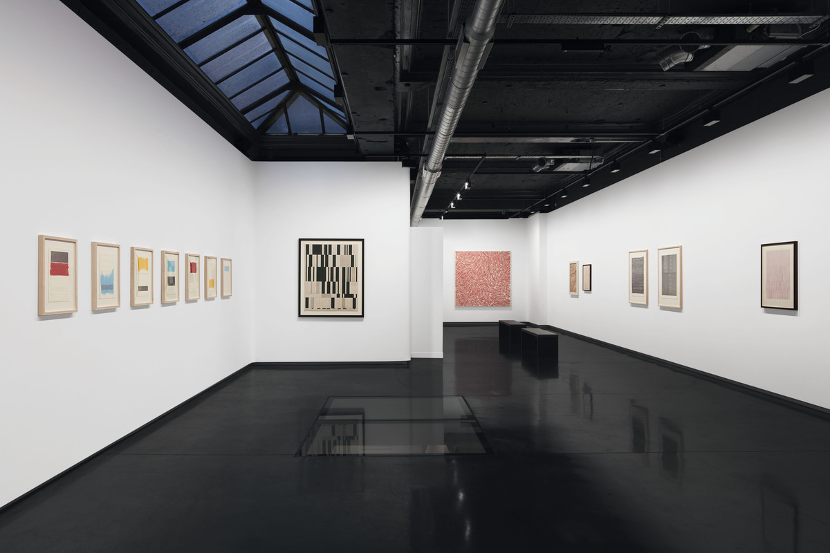 A photo of a white cube gallery with a black shiny floor, with lots of abstract works hanging on the walls