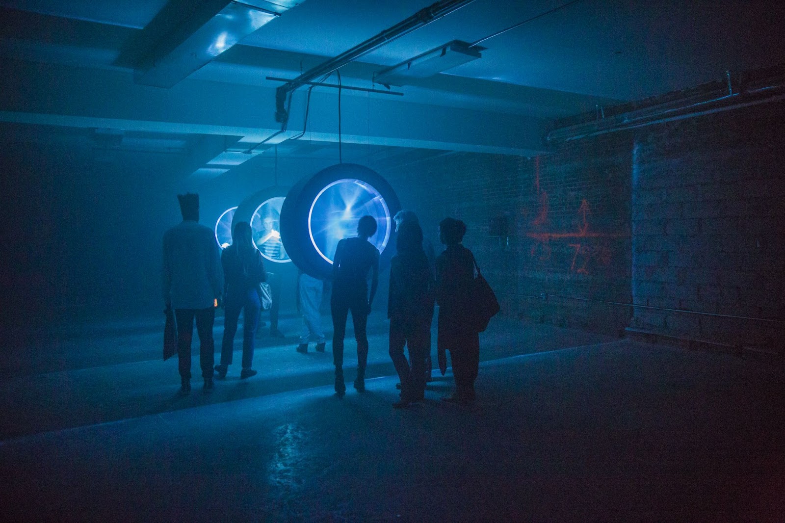 A photo of a gallery space with people standing around a blue circular light installation