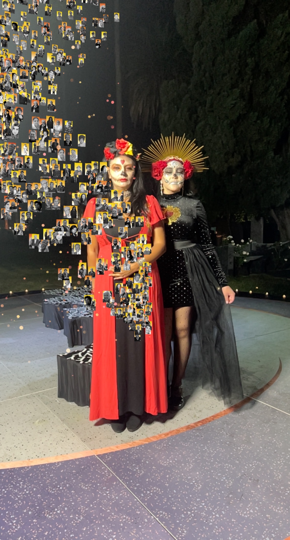 Two women wearing traditional costumes and makeup to celebrate the Day of the Dead stand amid a stream of small portraits in an augmented reality memorial