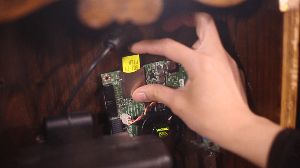 A hand places a catridge into a computer encased in a wooden cabinet