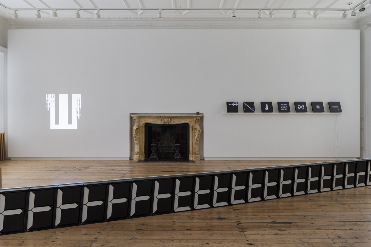 An install shot of a gallery space with an ornate fireplace at the center