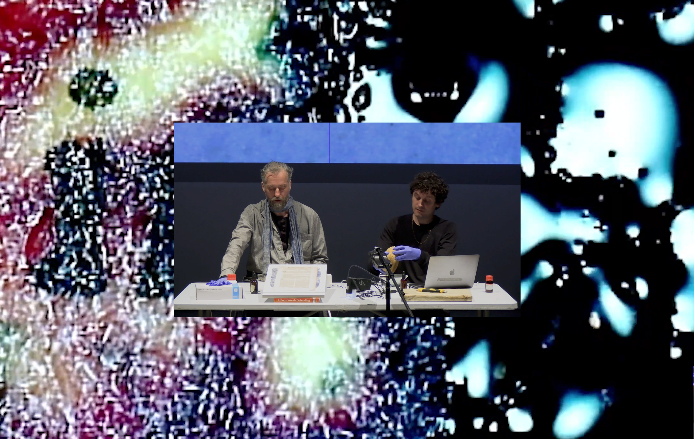 An image of two men giving a lecture superimposed onto a blurry abstract image 
