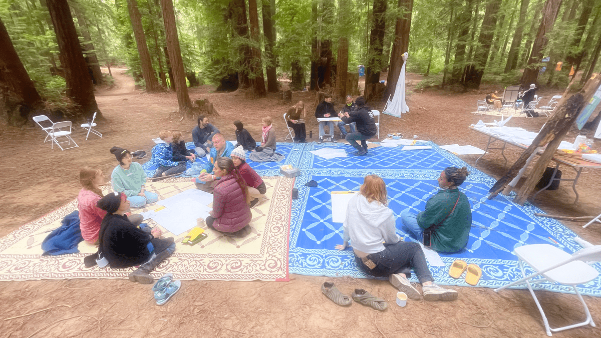 A photograph of people sitting on colorful blankets in a forest clearing