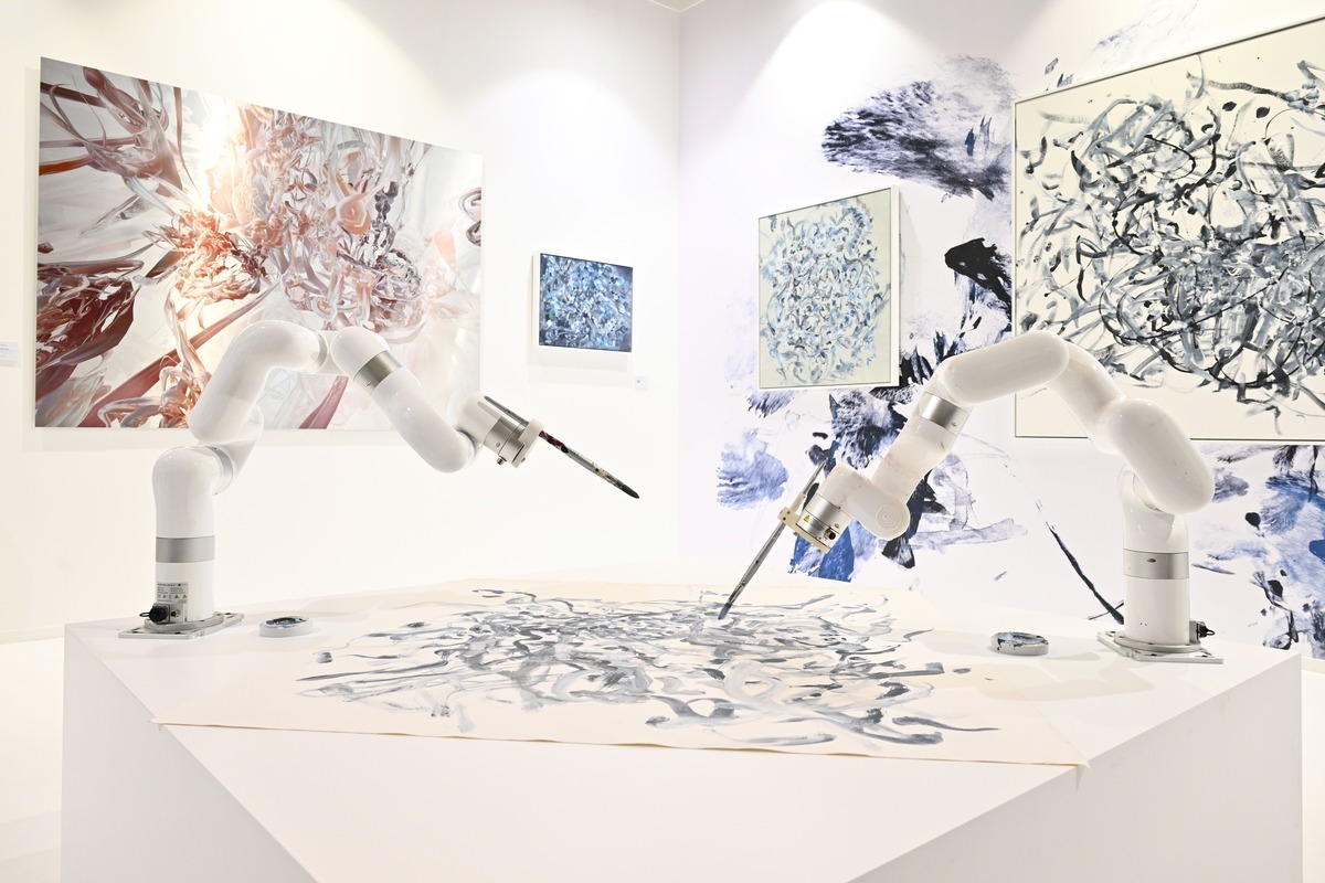 A pair of robotic arms mounted on a plinth manipulate paintbrushes to make an abstract work on paper.