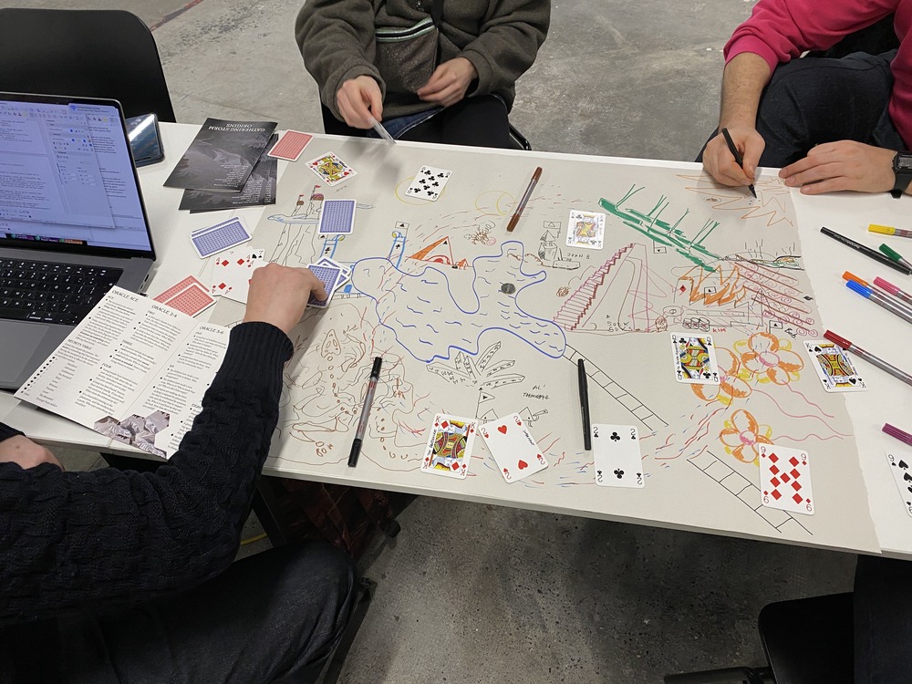 A photograph of people drawing an improvised map on a large piece of paper, littered with playing cards