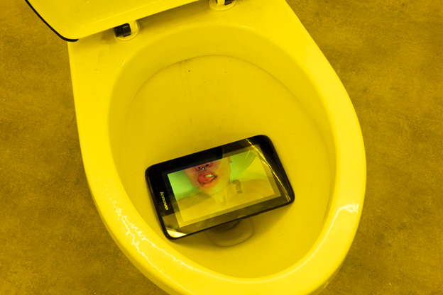 A photograph of a tablet in a toilet bowl, showing an image of a woman licking her lips