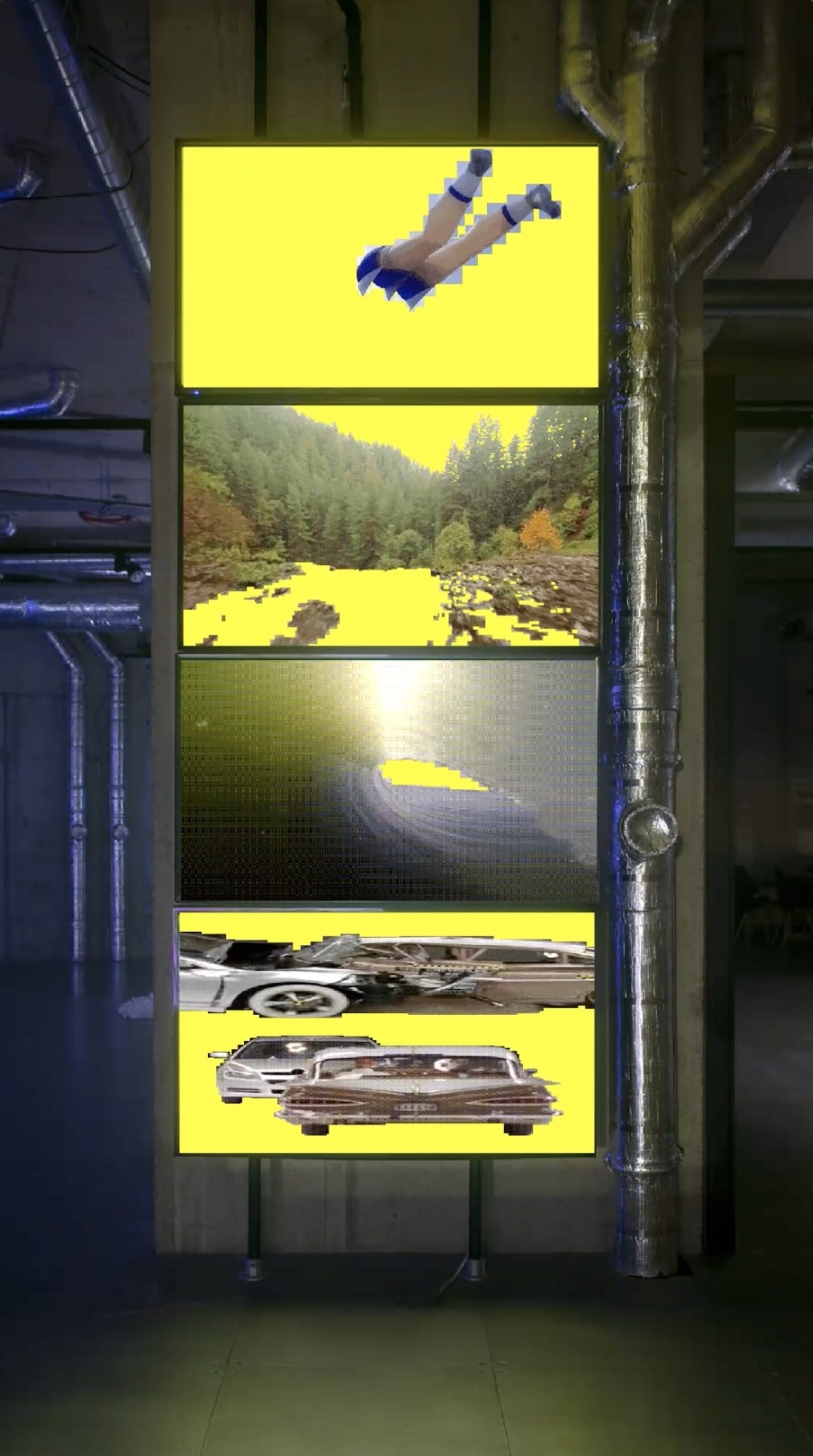 A photo of a video installation made up of four stacked flat-screen monitors each showing fragmented images on a bright yellow backdrop