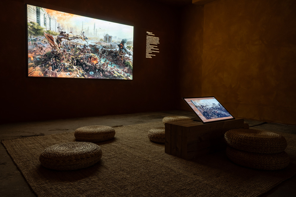 A photograph taken in a darkened room, where an image appears both as a large projection on a wall and on a smaller screen near the floor, with a navigable interface