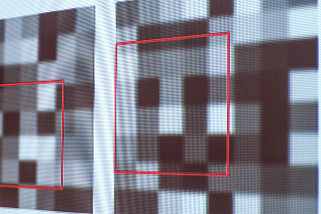 A close-up photo showing projections of squares made up of grayscale pixels with red boxes around face-like shapes picked up amid the pixels